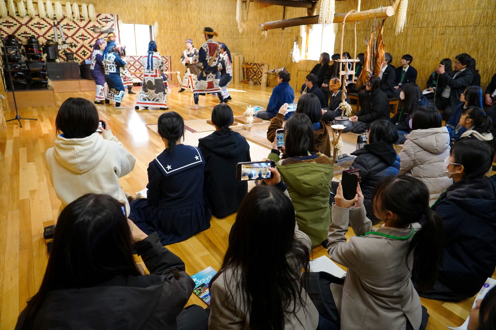 家屋チセの中で舞踊を鑑賞している